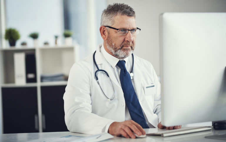 Médico sentado em frente a um computador usando um sistema para consultório