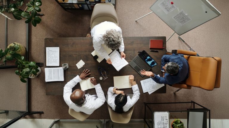 Reunião em clínica médica, com vários médicos em volta de uma mesa retangular, para delegar funções administrativas